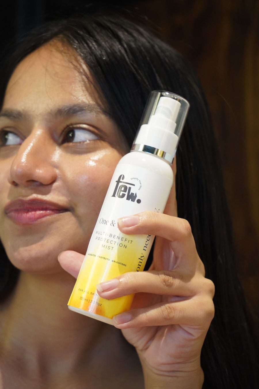 A woman holding FEW One & Done mist to her glowing cheek